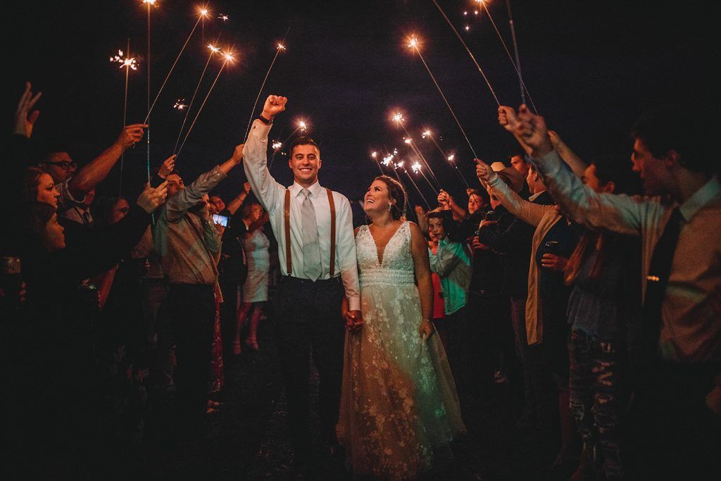 Newlyweds walk through a tunnel of sparklers held by guests at a night wedding.