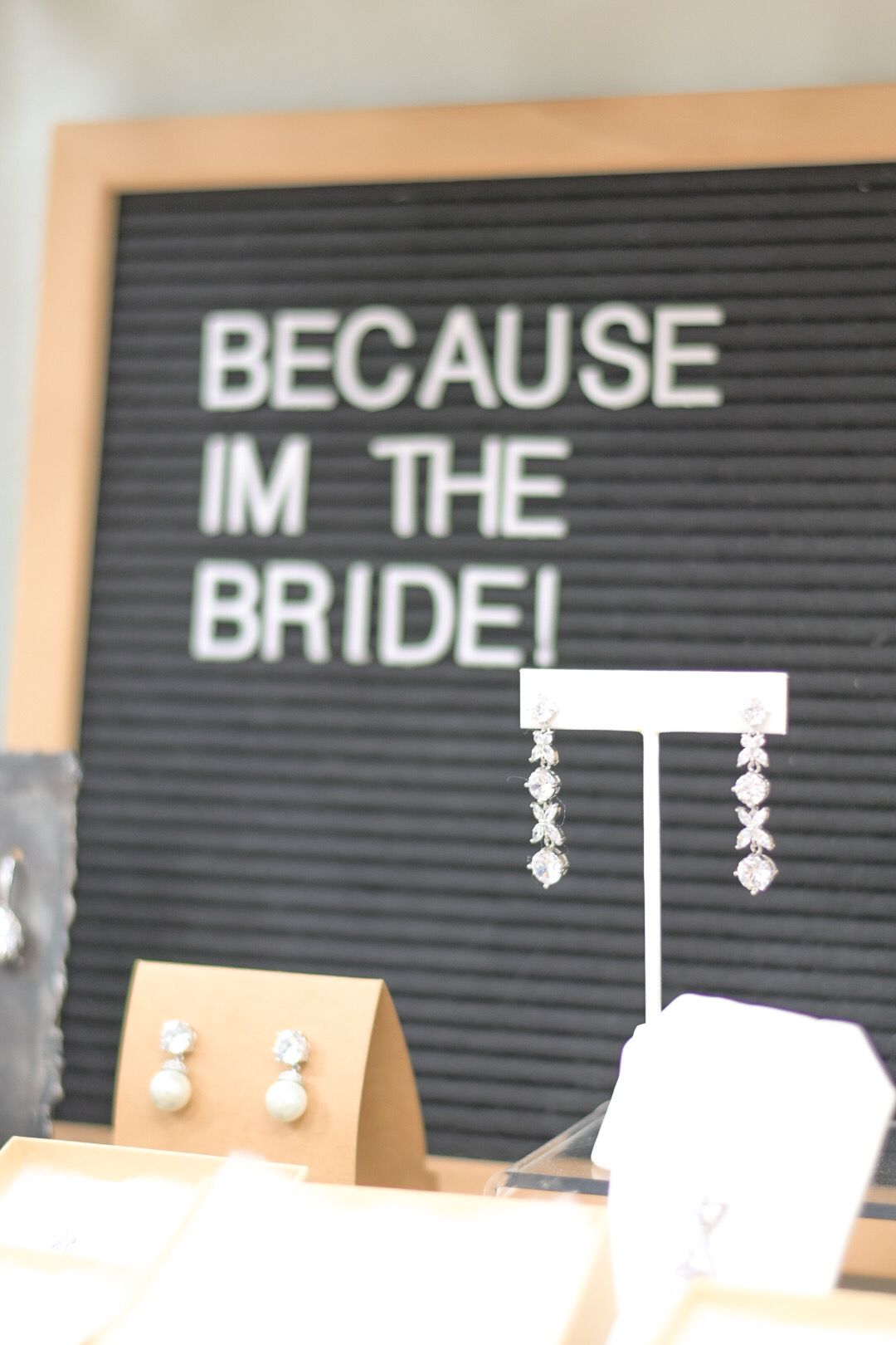 Woman in a white off-the-shoulder wedding dress, hands on hips, posing by a window.