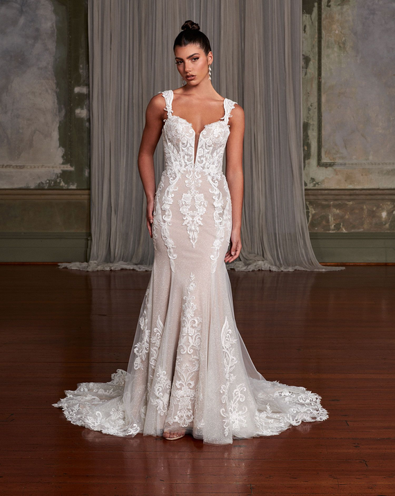 Woman in wedding dress stands in doorway, arms outstretched.