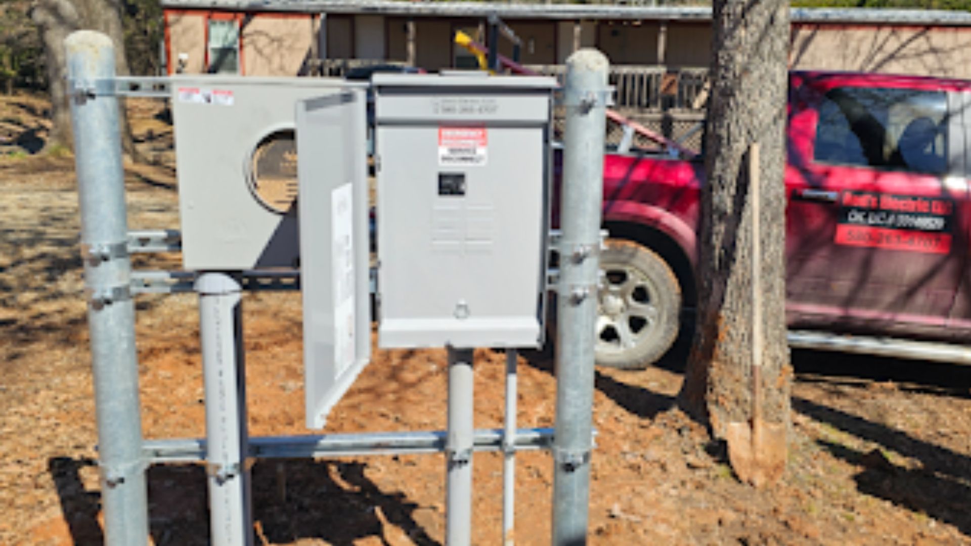 Gray electrical panel mounted on wooden posts beside a red SUV in a wooded outdoor area