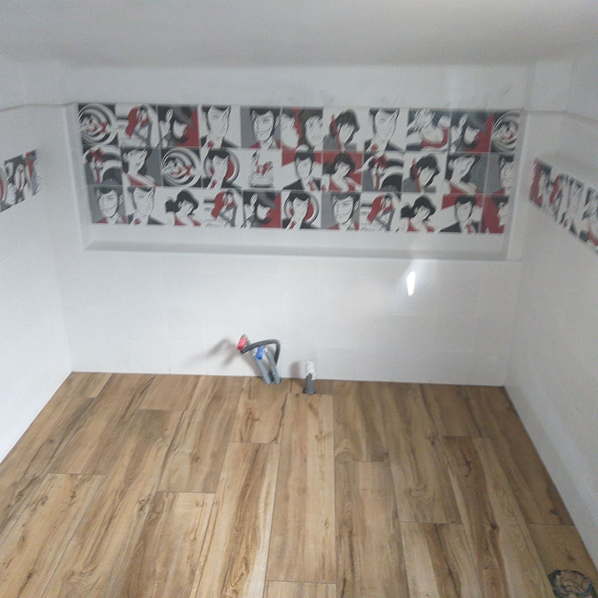 Stanza vuota con pavimento in legno, pareti bianche e un pannello decorativo a parete nero, bianco e rosso.