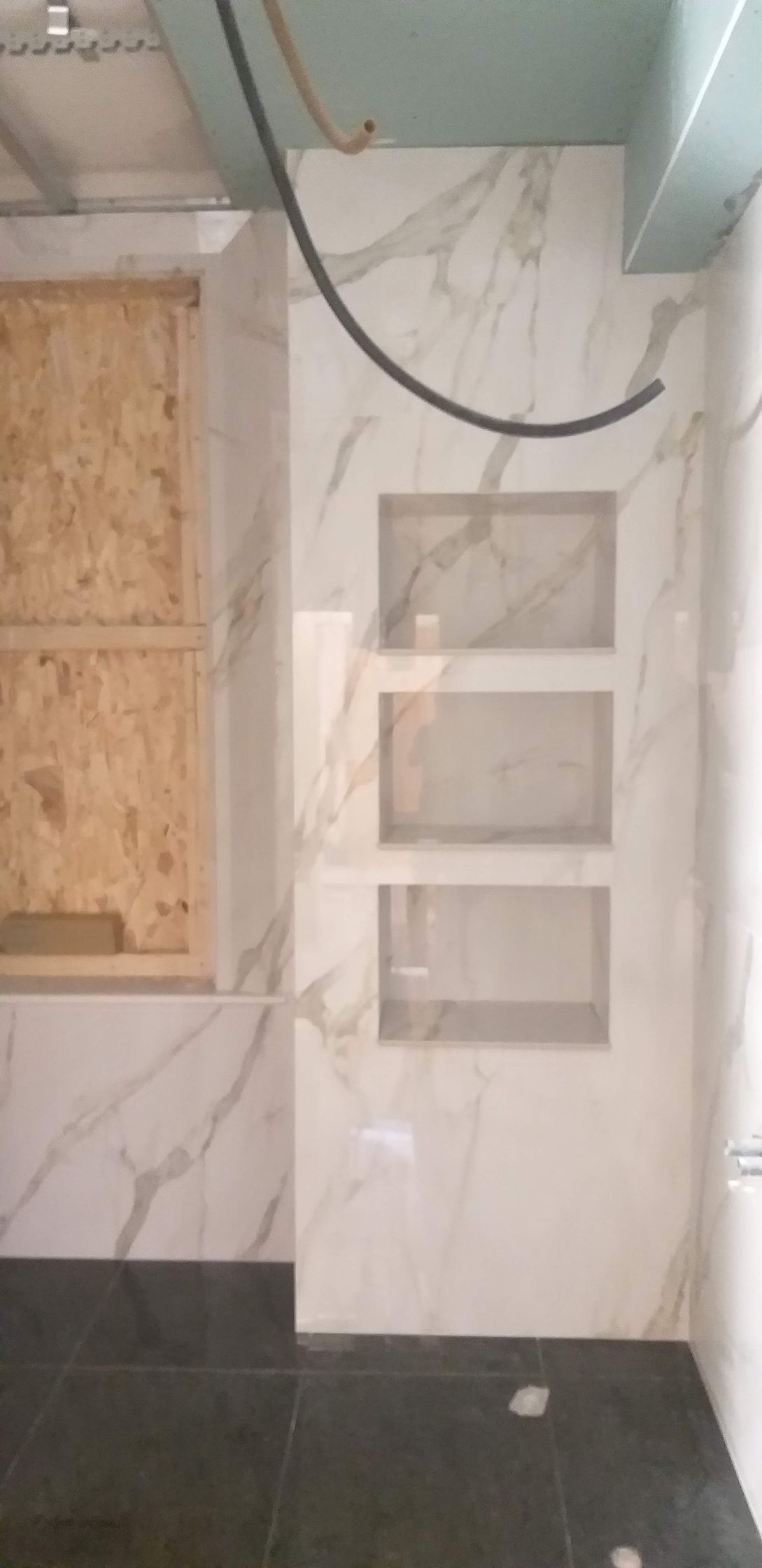 Parete parzialmente piastrellata con quattro mensole a incasso e cavi elettrici a vista in un interno non rifinito.