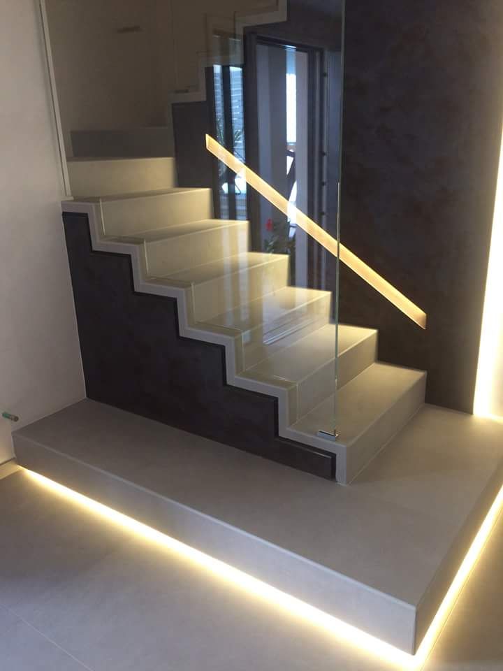 Scala interna moderna con gradini illuminati, parete scura e illuminazione a LED lungo il bordo del pavimento.