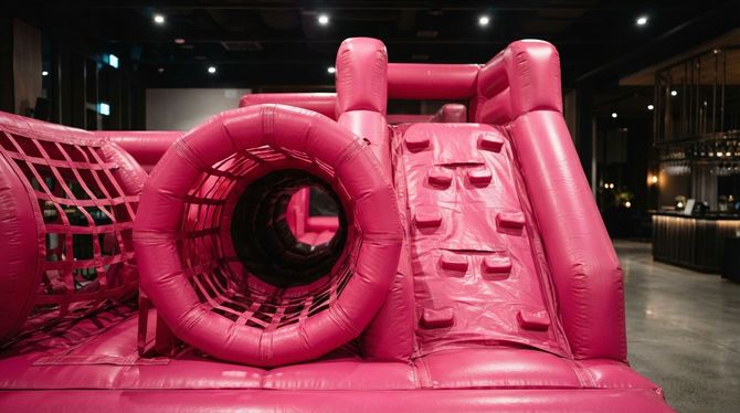 Bright pink inflatable obstacle course with slide and tunnel indoors