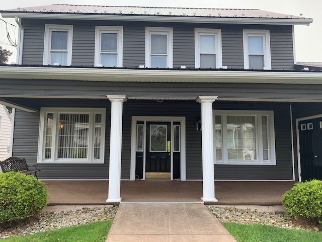 Gray two-story house with white columns, windows, and front door. Green bushes and grass.