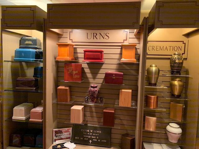 Display of cremation urns in various colors, materials, and styles, labeled