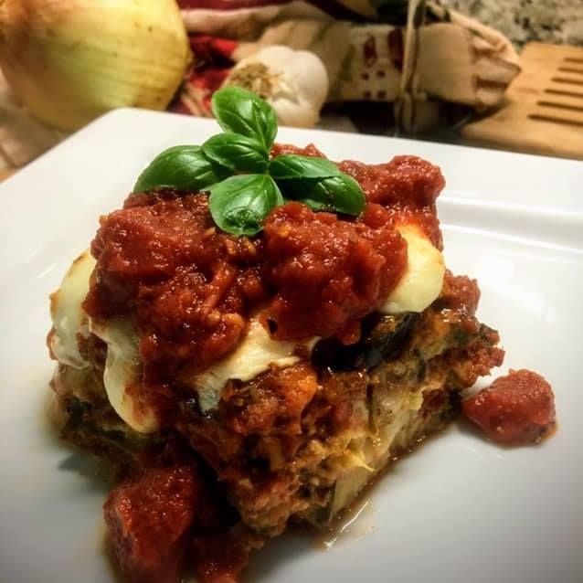 A slice of lasagna with tomato sauce and basil on a white plate