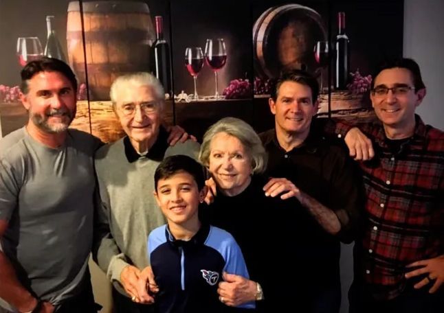 A family posing for a picture in front of a painting of wine bottles and glasses
