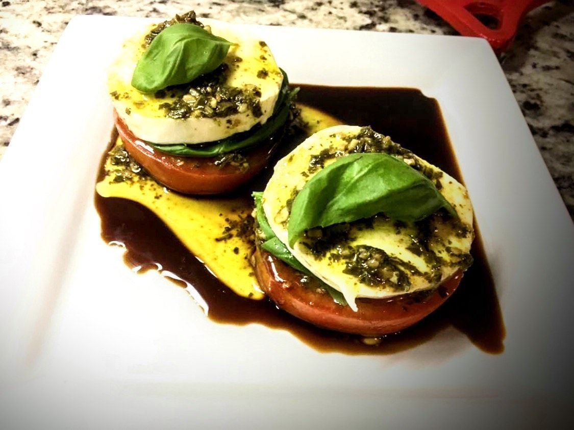 A white plate topped with tomatoes mozzarella and basil