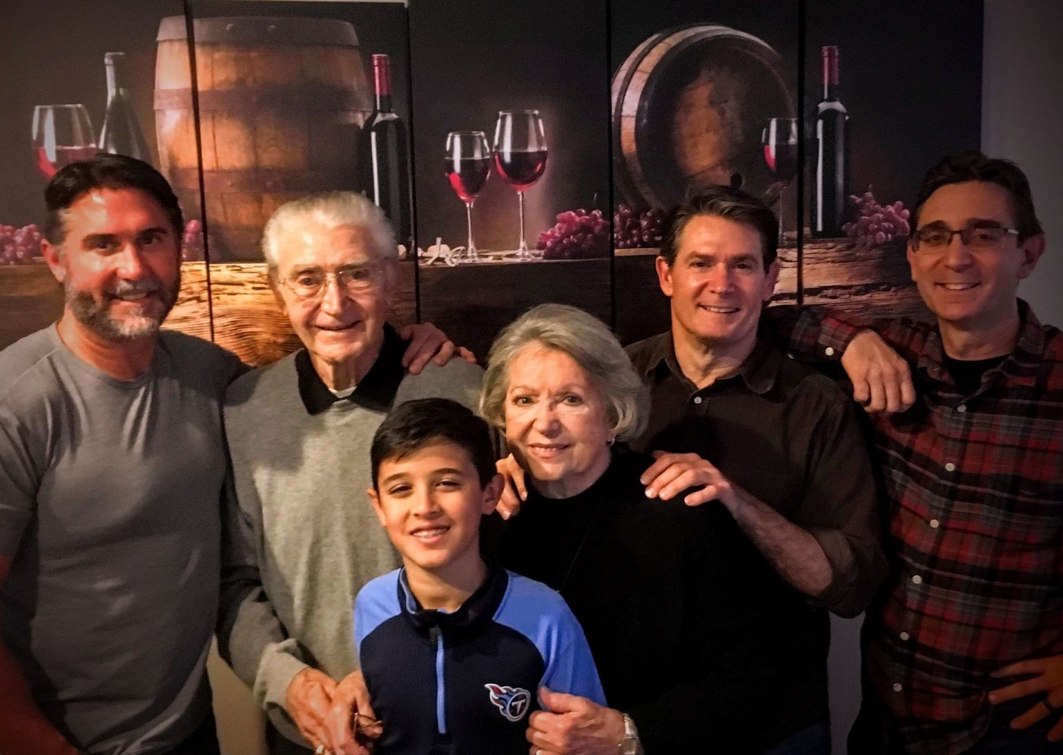 A group of people posing for a picture with a picture of wine barrels in the background