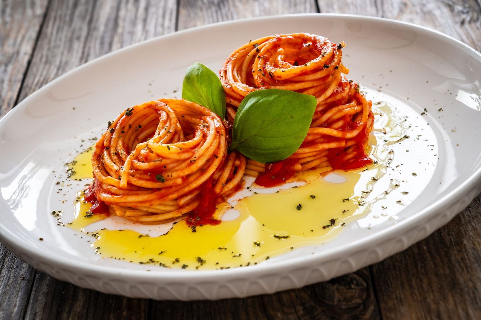 A plate of spaghetti with tomato sauce and basil on a wooden table.