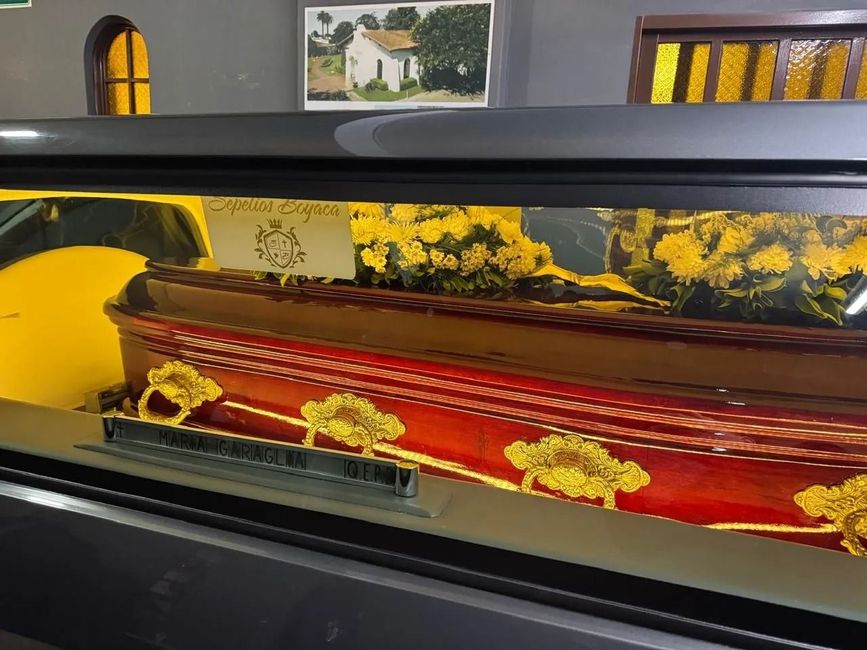 Ataúd abierto con forro floral rojo y dorado en un entorno funerario.