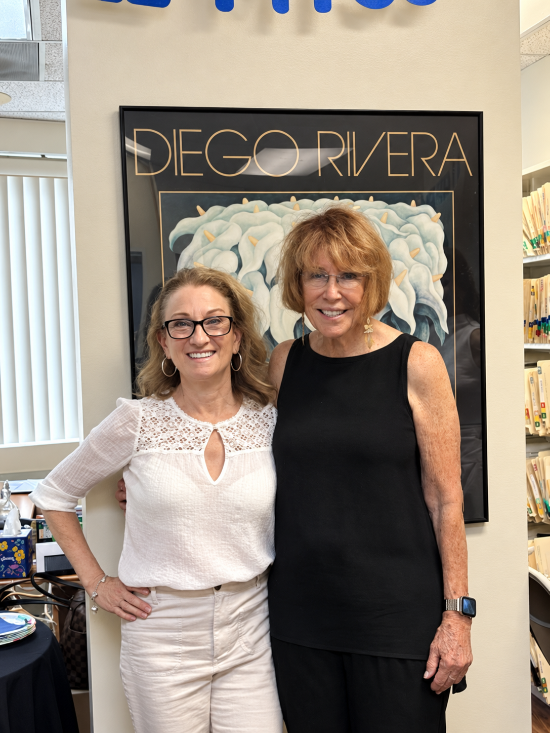 Two women smiling in front of a DECO RIVERA art display.