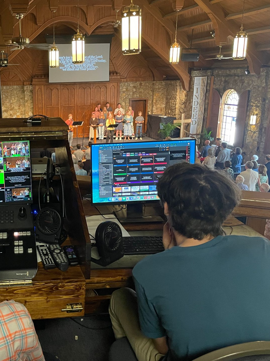 Person sitting in front of a computer screen with the slides for a church worship service, happening below.
