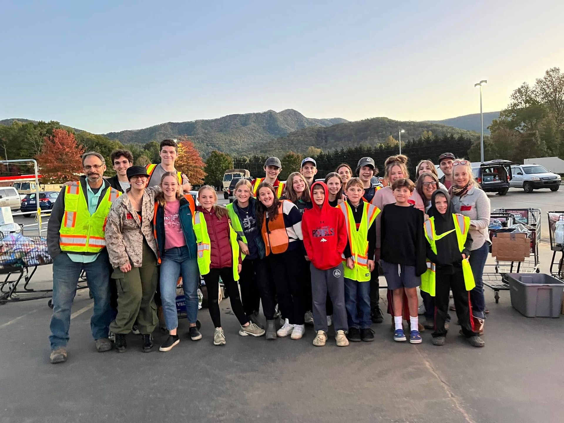 Group of people in neon safety vests posing outdoors at dusk, with hills and parked cars in the background