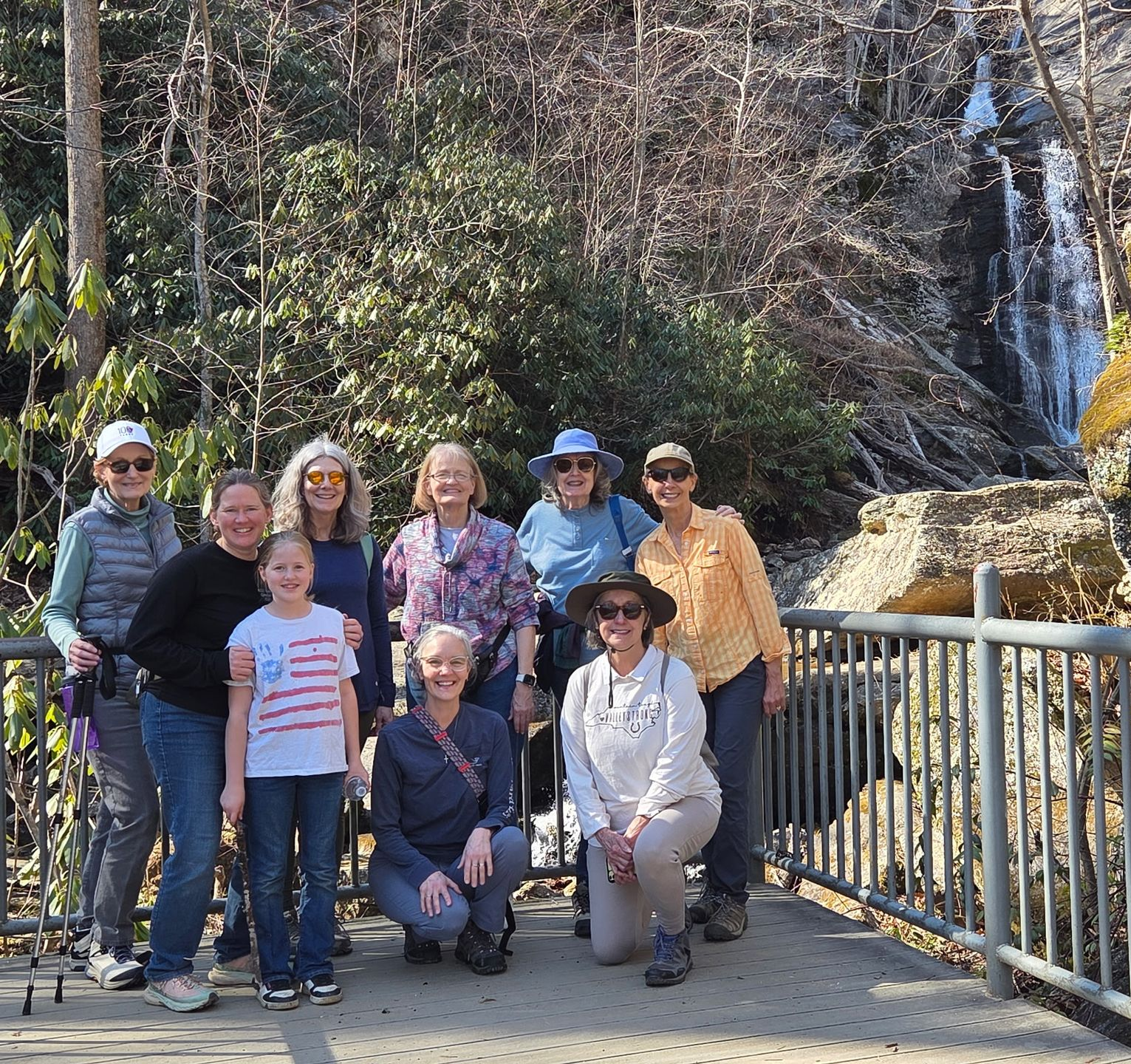 Group posing on a viewing platform with a waterfall and forest in the background.