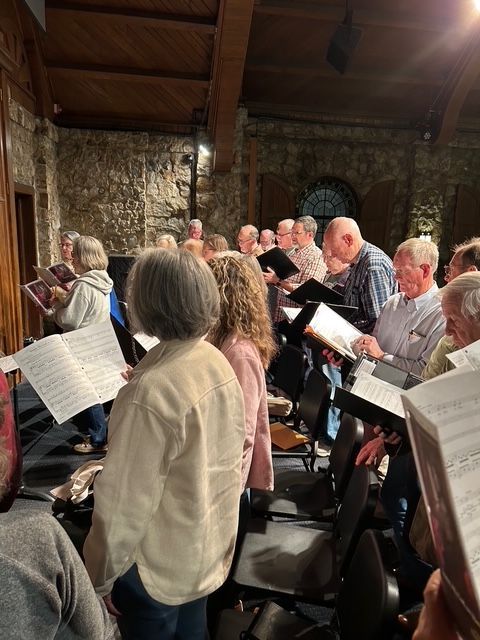 A group of people with choir books gathered in a rehearsal space.
