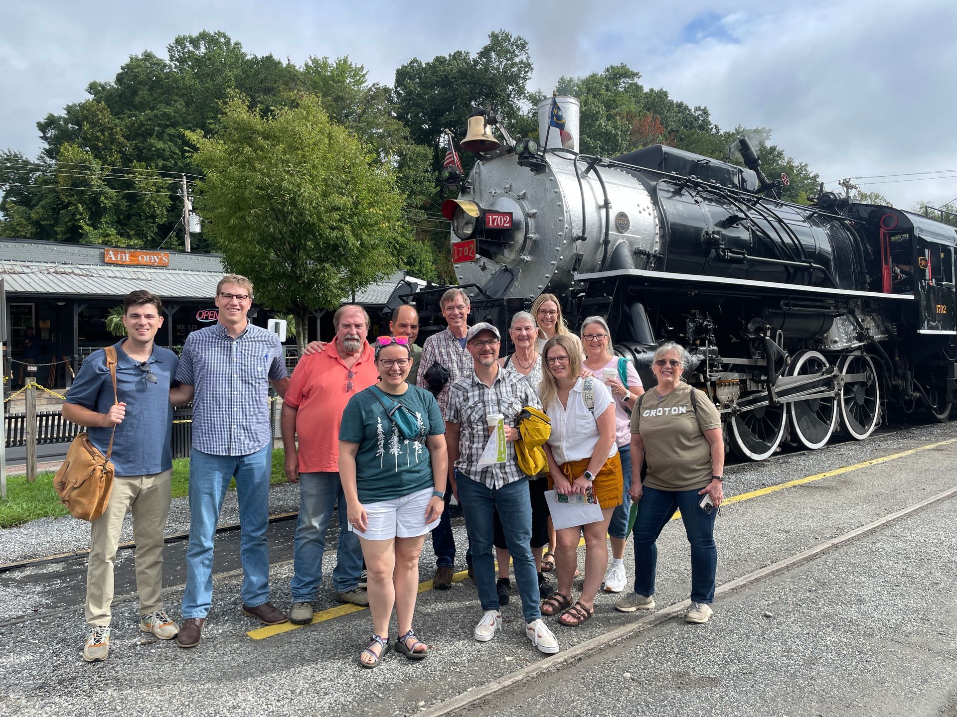 Group of people standing in front of a steam engine.