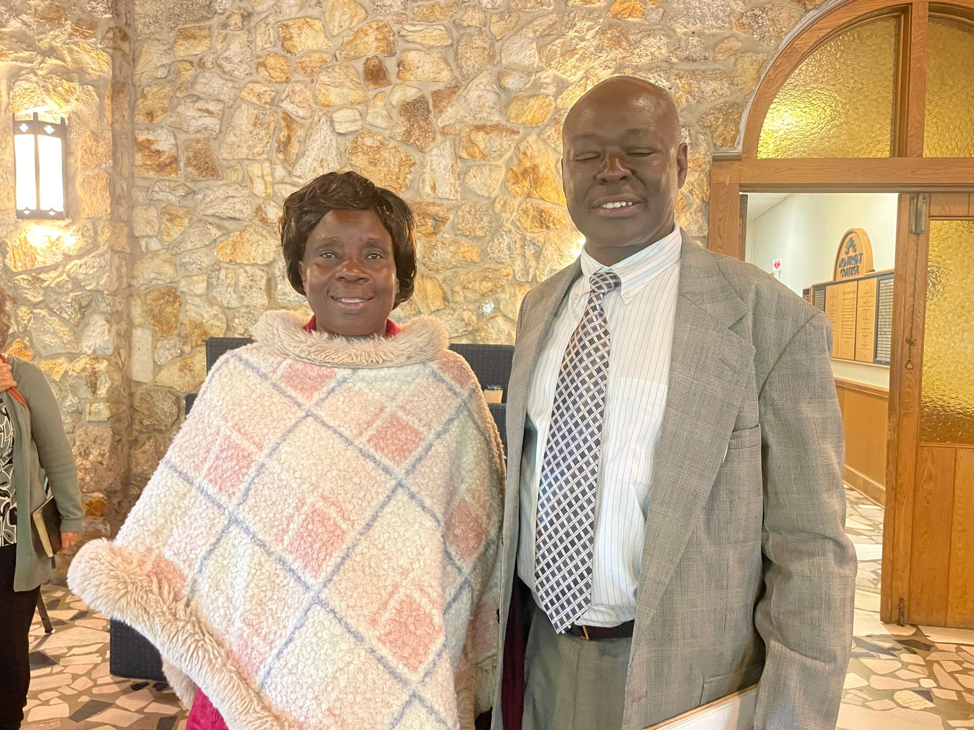 Man and woman standing in a room in front of a stone wall.