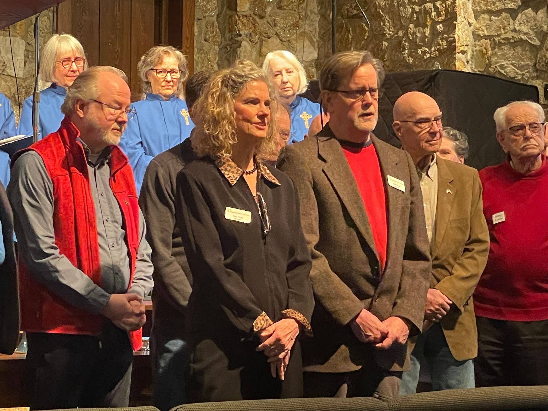 Several people stand together indoors, wearing formal attire in front of a stone wall.