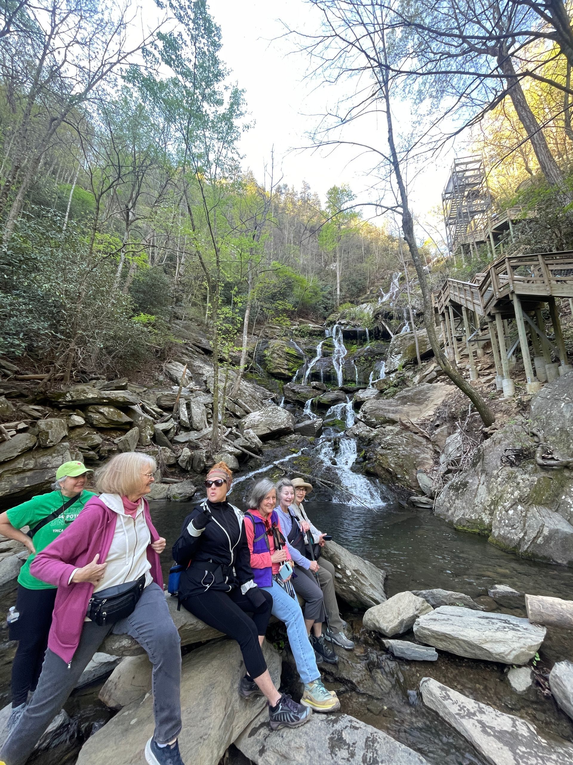 Group sitting on rocks beside a small waterfall in a wooded creek area