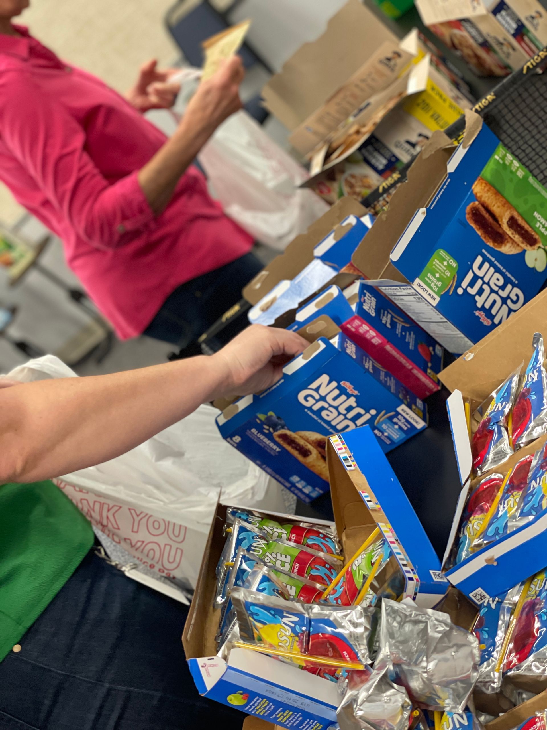 Hands reaching into a box of assorted  snacks on a table.