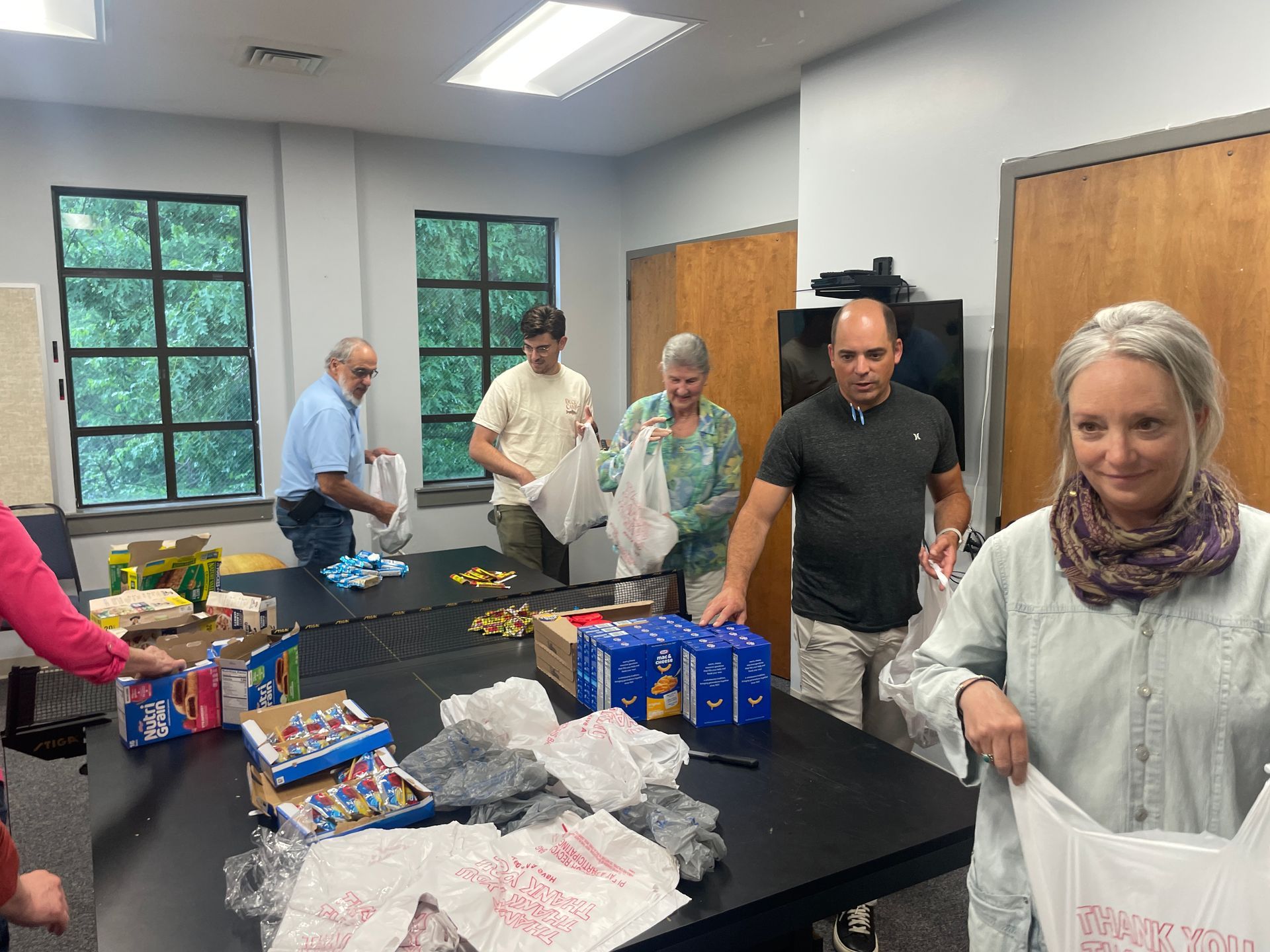 People sorting snacks on a table in a bright room with windows and wooden doors
