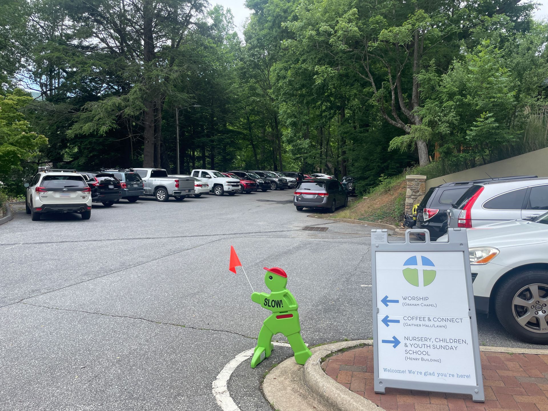 Parking lot with a green slow down sign and a directional board near parked cars and trees.