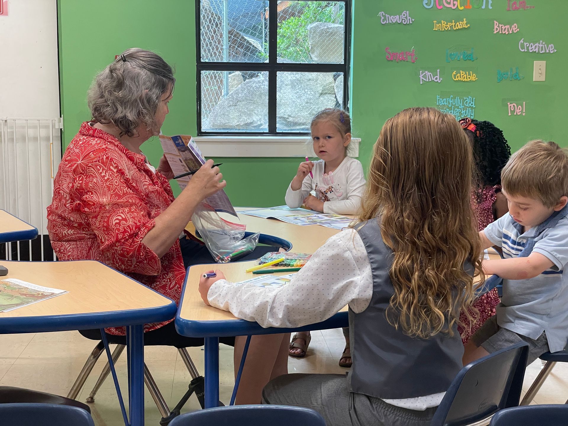 Teacher and children sitting around a table in a classroom, engaged in a group activity.