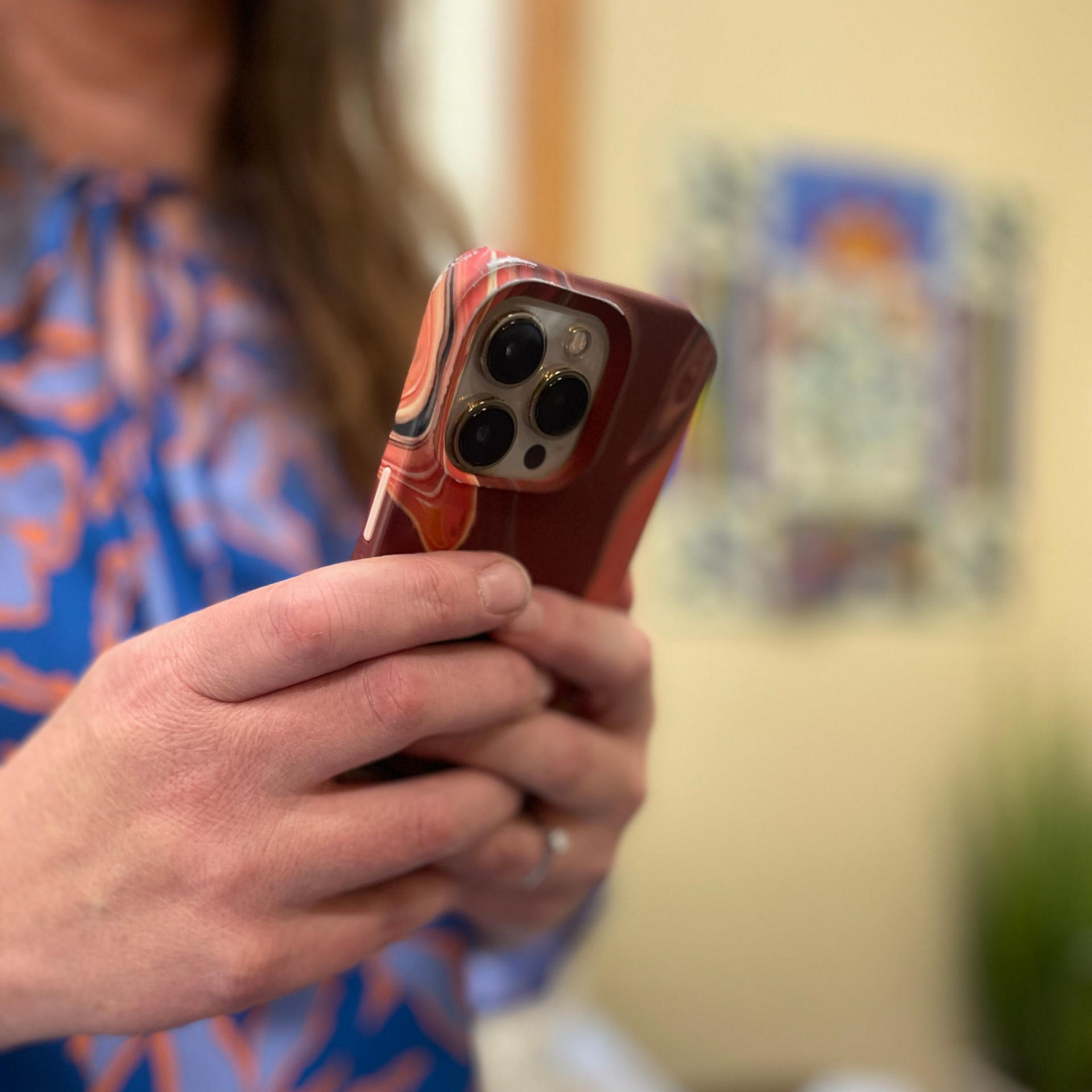 Hands holding a red smartphone in a blurred indoor setting