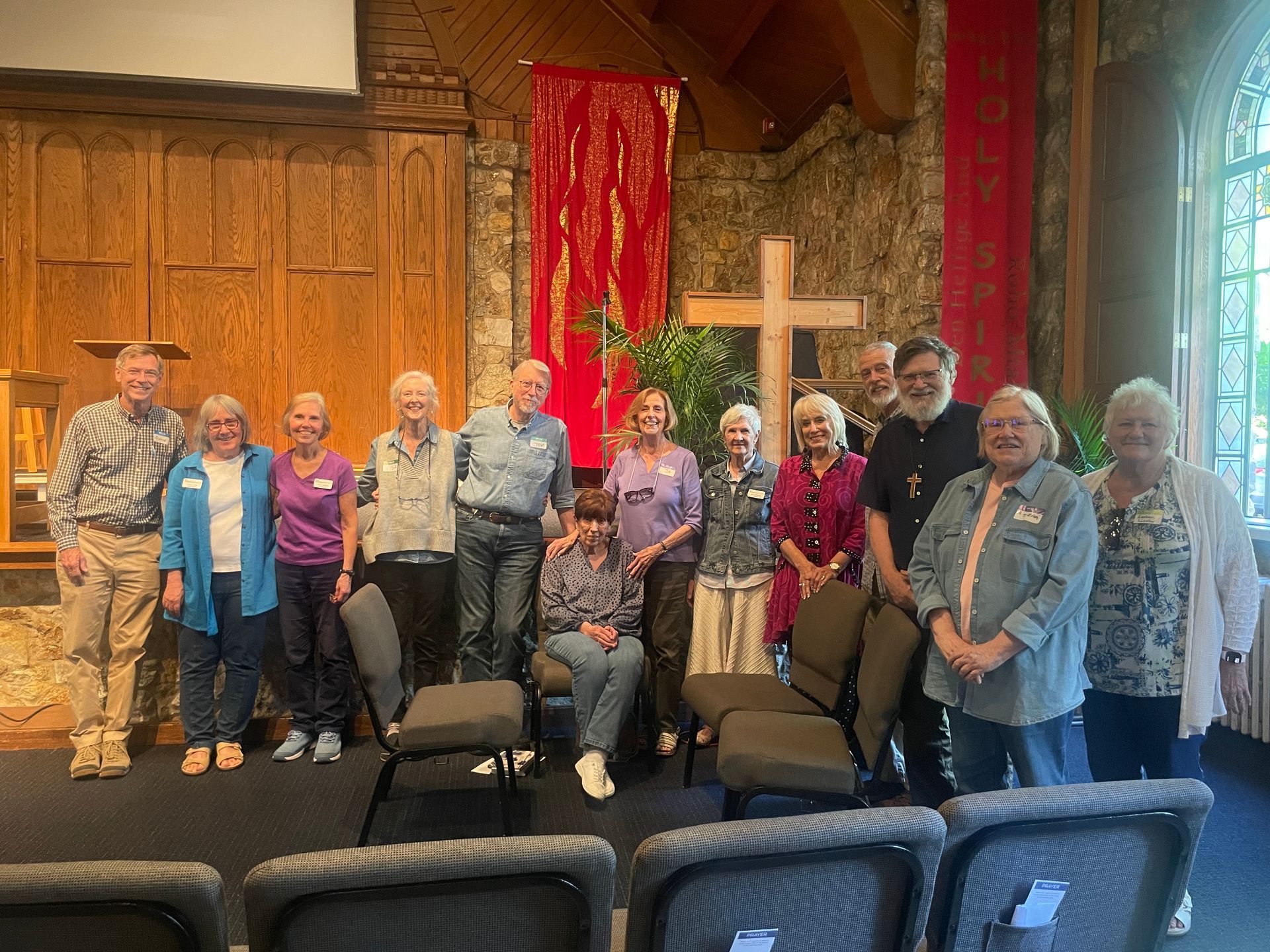 Group posing in a church interior with red drapes and a cross in the background.