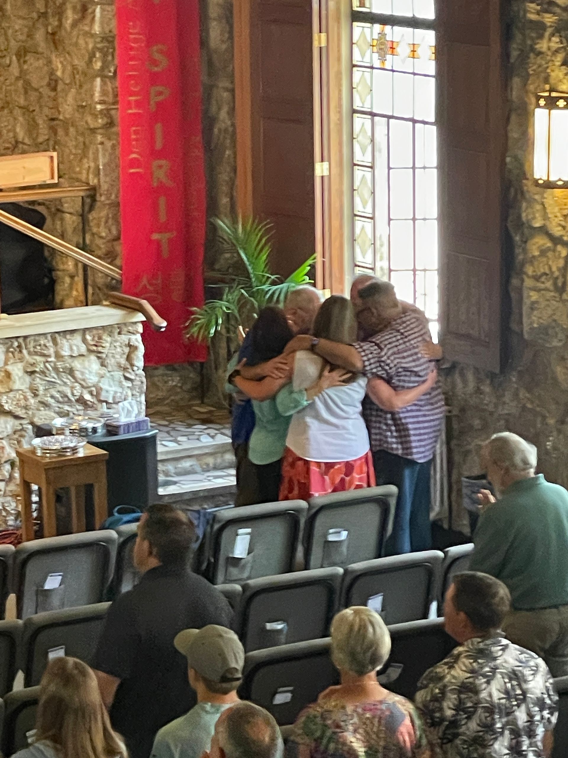 Group of people huddled together praying with their arms around each other during a church service.