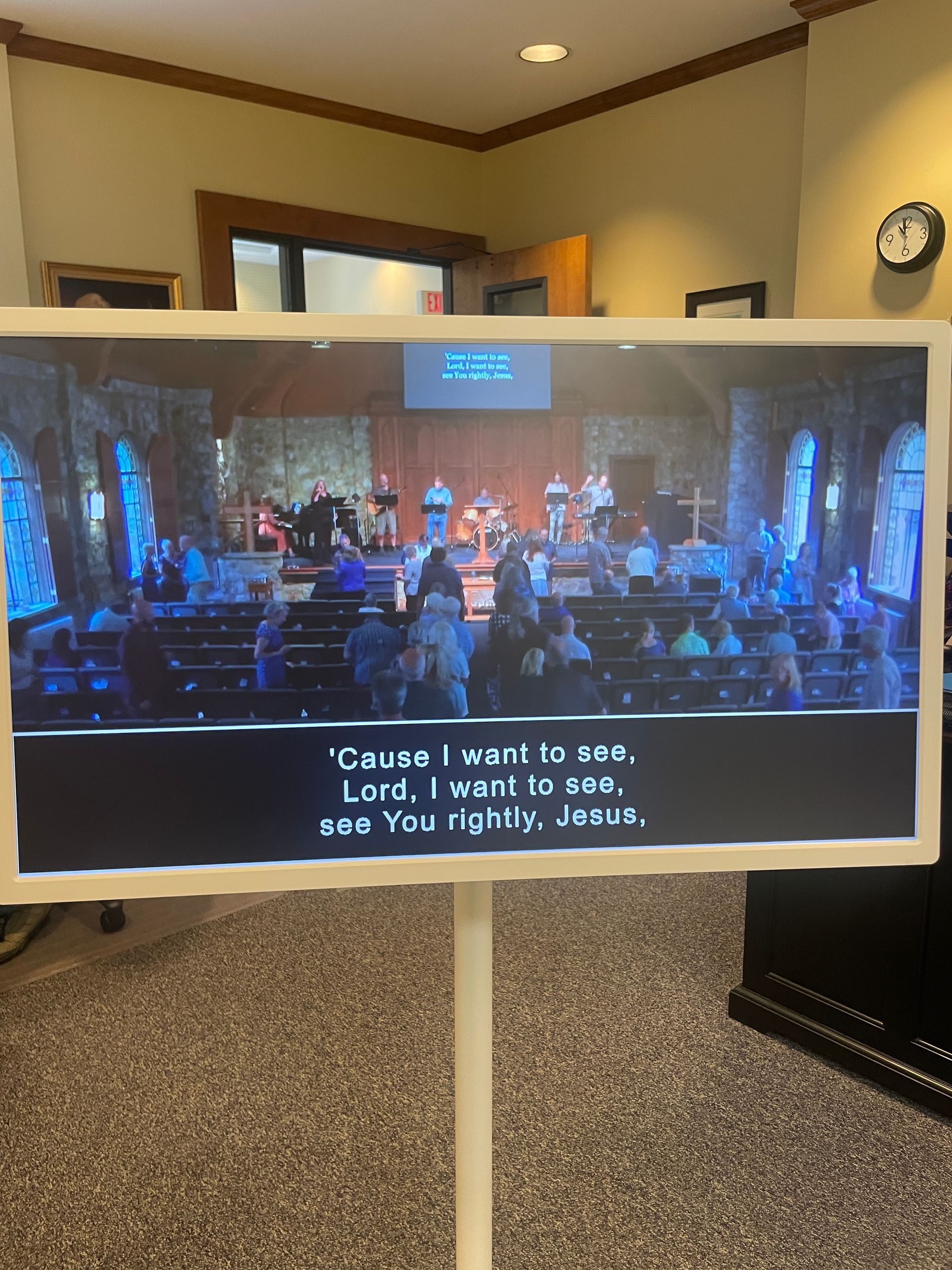 A TV displaying a stage performance with subtitles, in a room with beige walls and carpet.