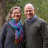 Man and woman stand in front of greenery.