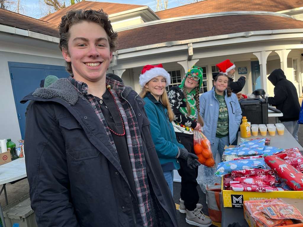 Youth smiling at an outdoor table with food and drinks, two wearing Santa hats.