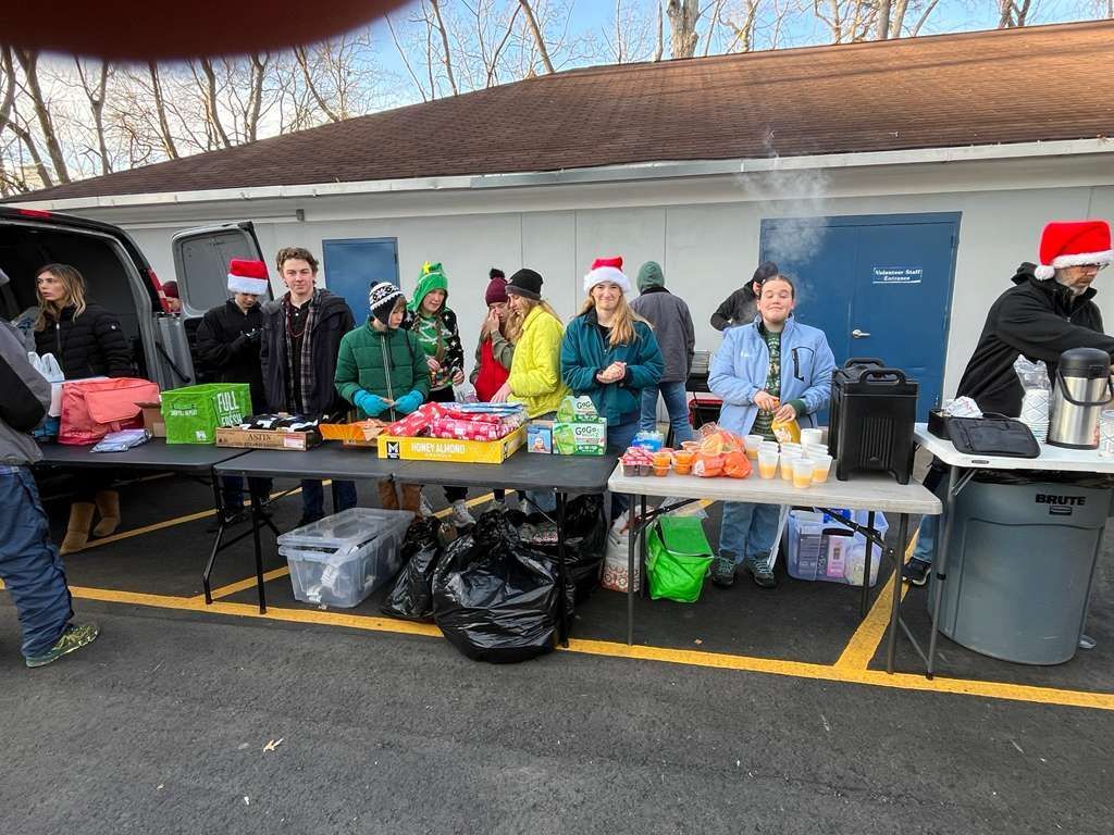 People gathered at outdoor tables with food and drinks in a parking lot.