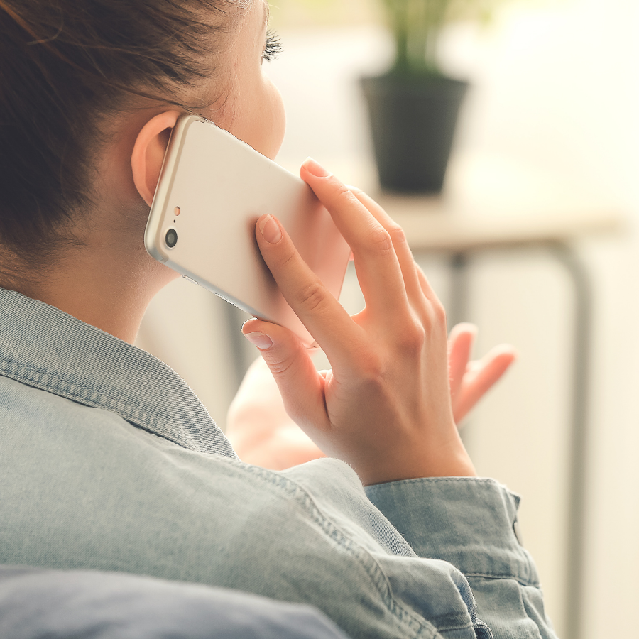 Person holding a white smartphone to their ear, seen from behind in a bright indoor setting