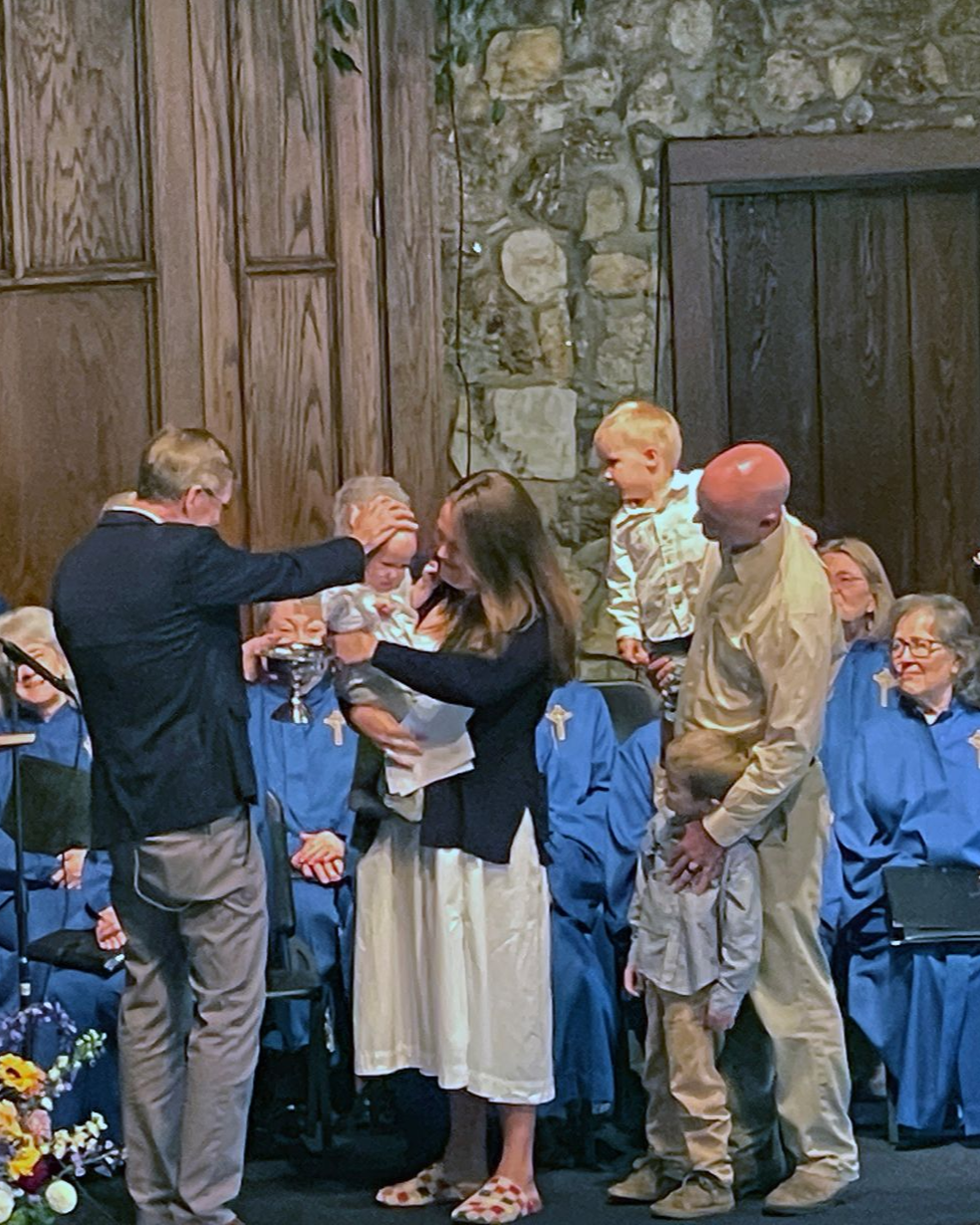 A family with three children, one being held by mom while being baptized.