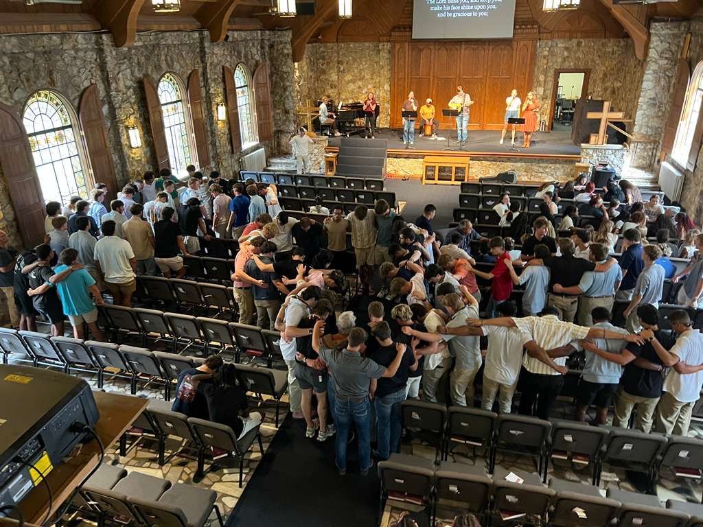 College students gathered in a stone chapel for worship - gathered arm in arm to pray and worship.