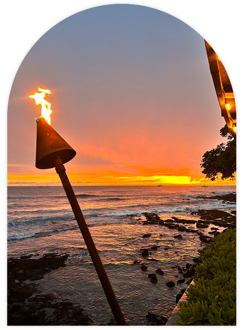 A tiki torch burning brightly against a vibrant sunset over the ocean.