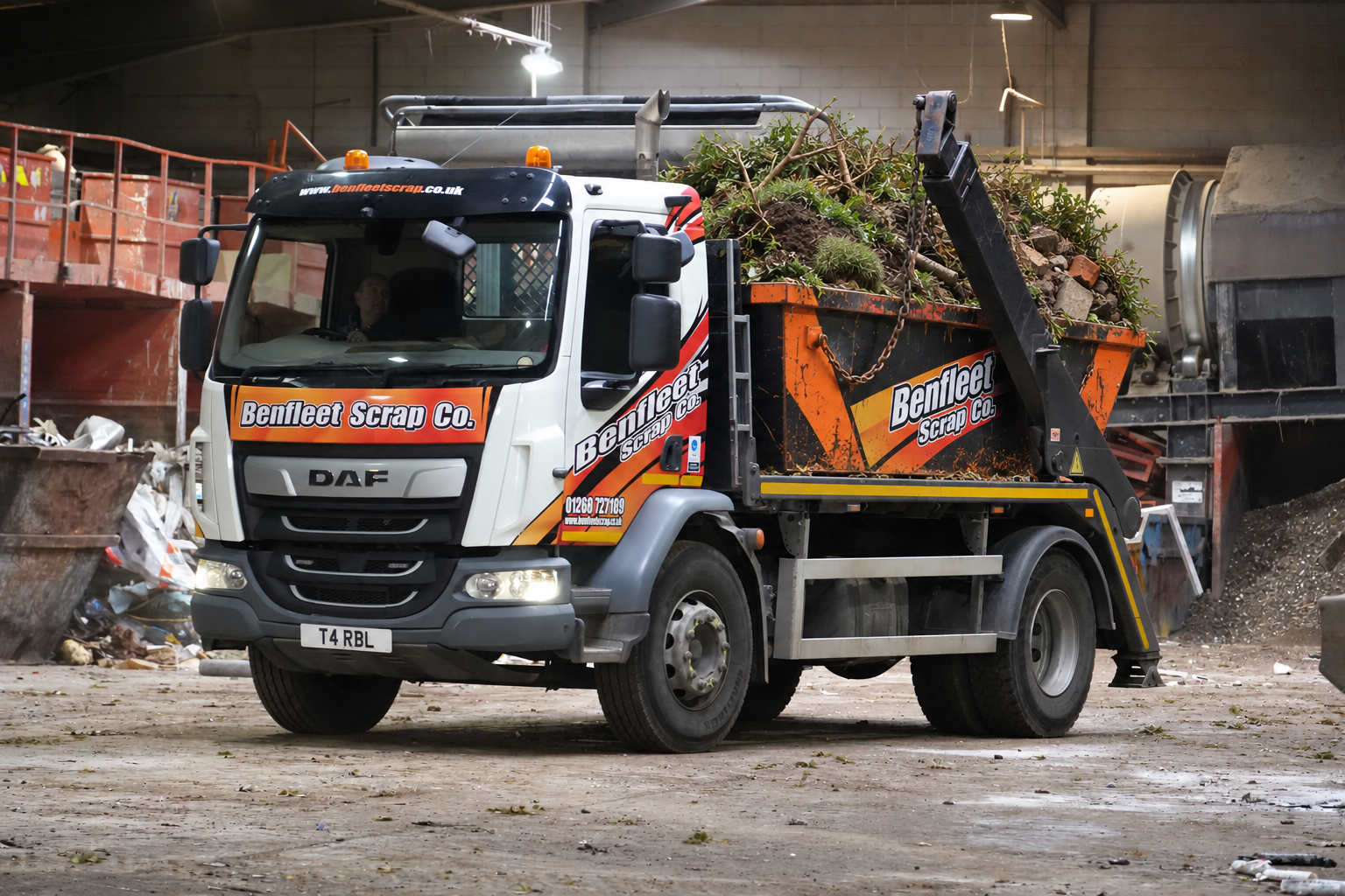 Orange-and-white skip loader truck carrying green yard waste inside a warehouse yard