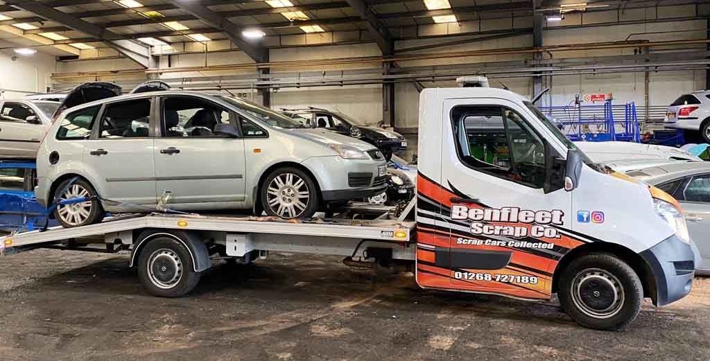 A Benfleet Scrap tow truck is carrying a car on the back of it.