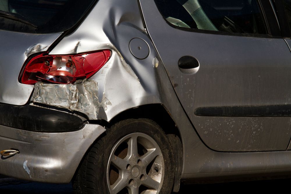 A silver car with a damaged bumper and tail light