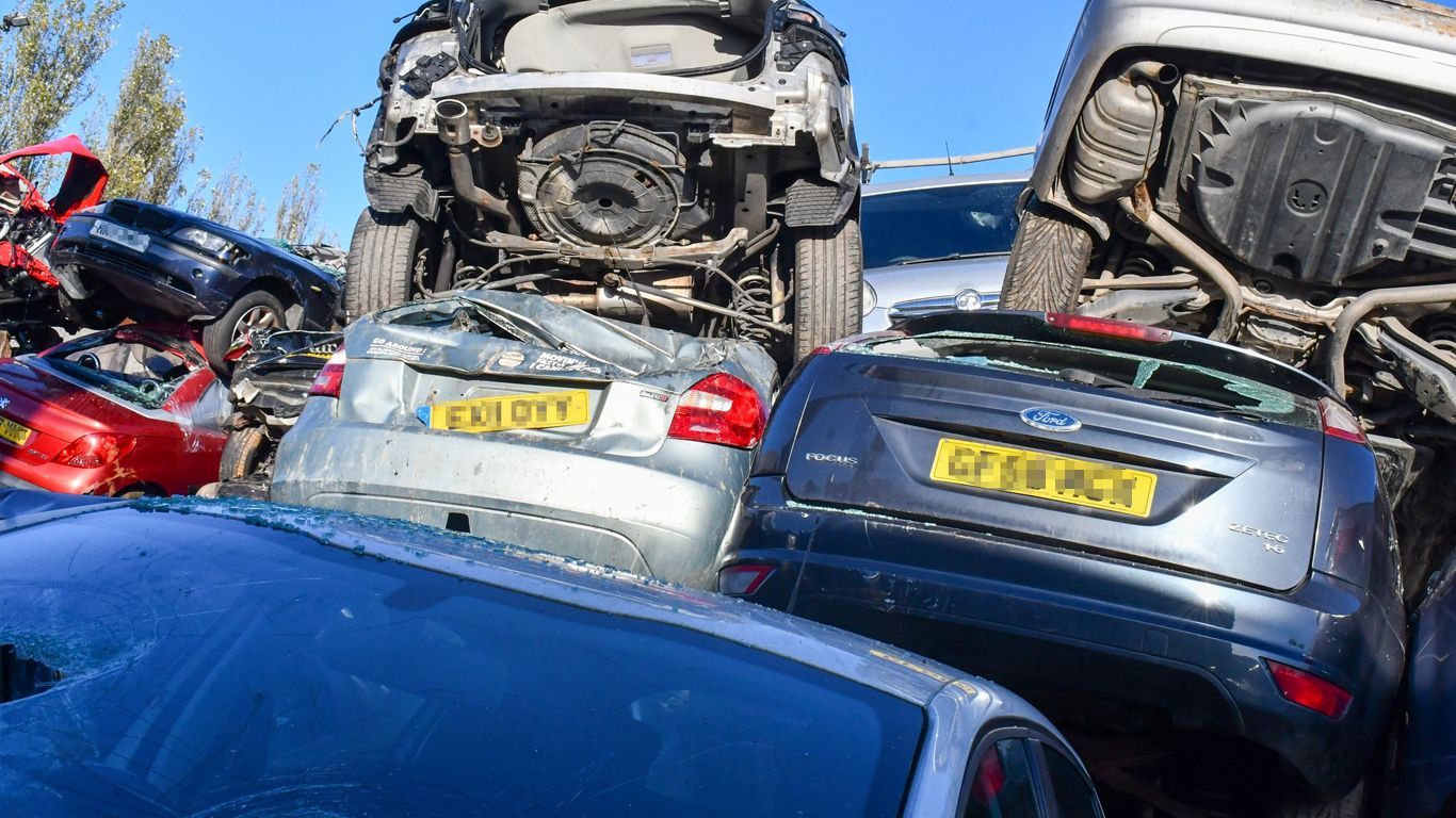 A bunch of cars are stacked on top of each other in a scrap yard.