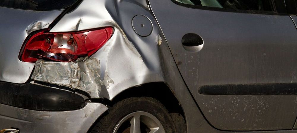 A silver car with a damaged rear end is parked on the side of the road.