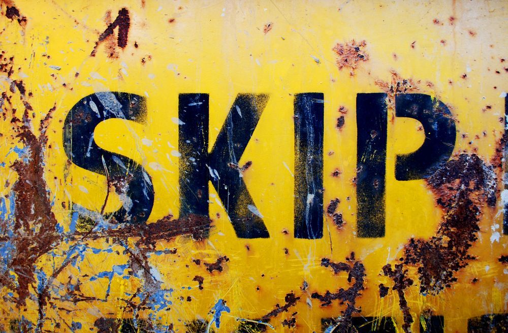 A rusty yellow sign that says skip on it