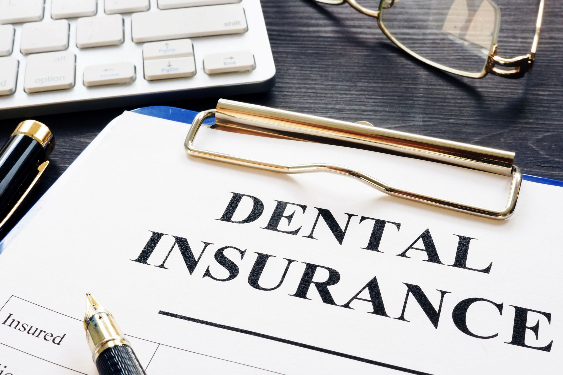 Dental insurance form on a clipboard with a keyboard, glasses, and pen.