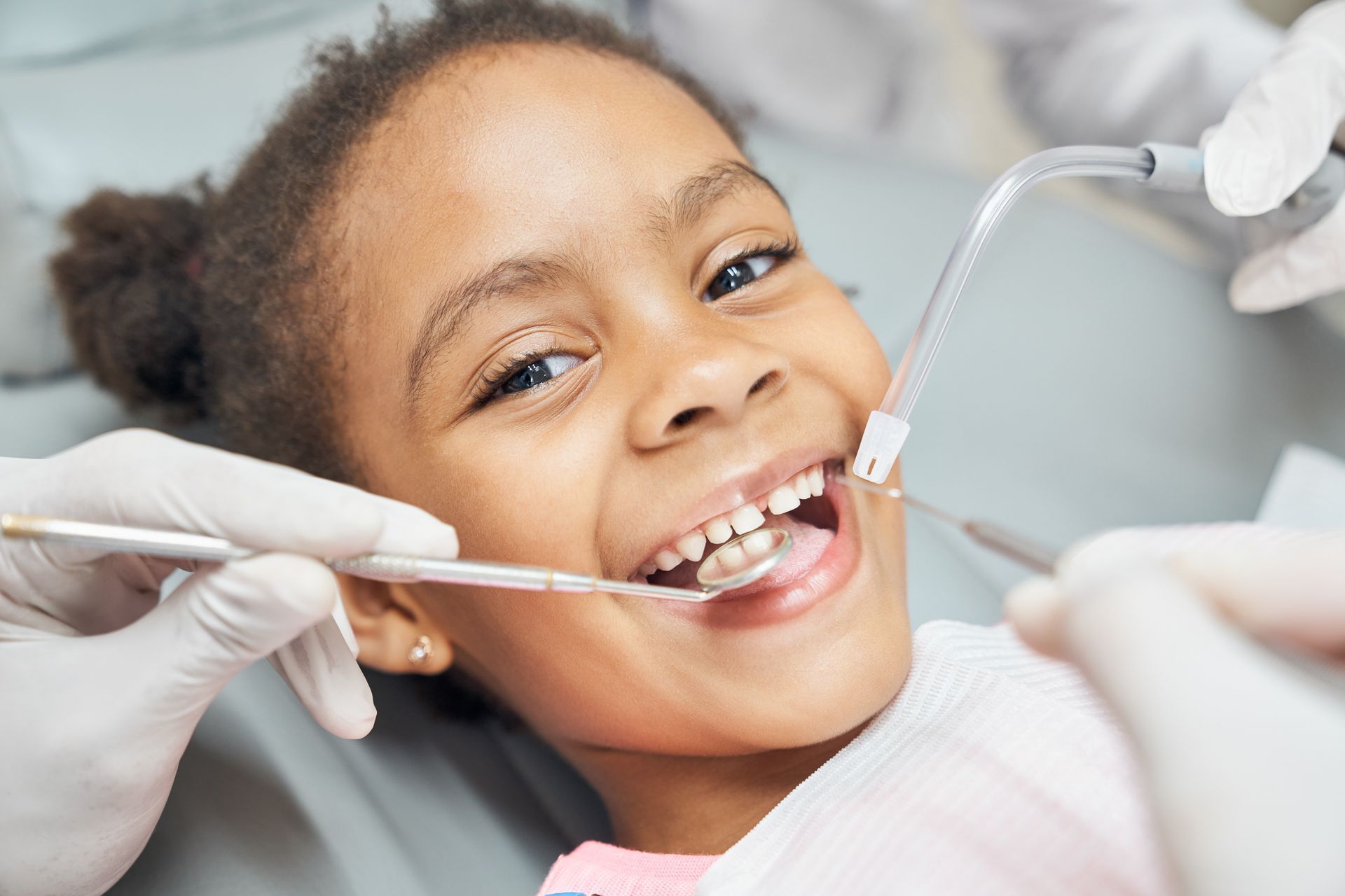 Young child at dentist appointment, smiling with mouth open. Dentist tools visible.