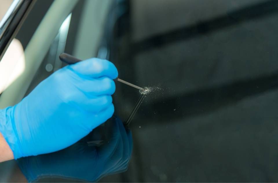 Blue-gloved hand applying adhesive to a car windshield with a small tool
