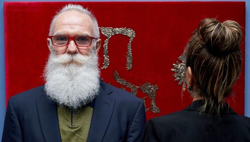 Dos personas observan una vitrina roja con elaboradas cadenas de plata y decoraciones florales.